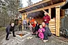 Gruppe menneske samla ved bålplass framfor ei nybygd gapahuk i skogen.